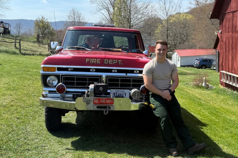 Danny Wells sits on the front fender of a fire department truck.