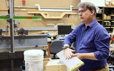 A professor holds a sample of wood in an lab with testing equipment