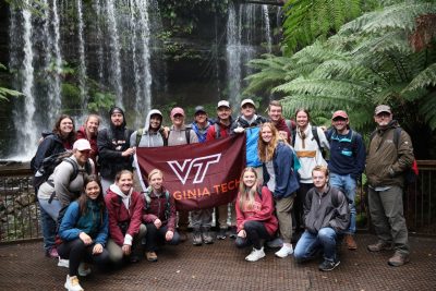 Students and a professor in front of a waterfall holding a flag with the Virginia Tech logo.