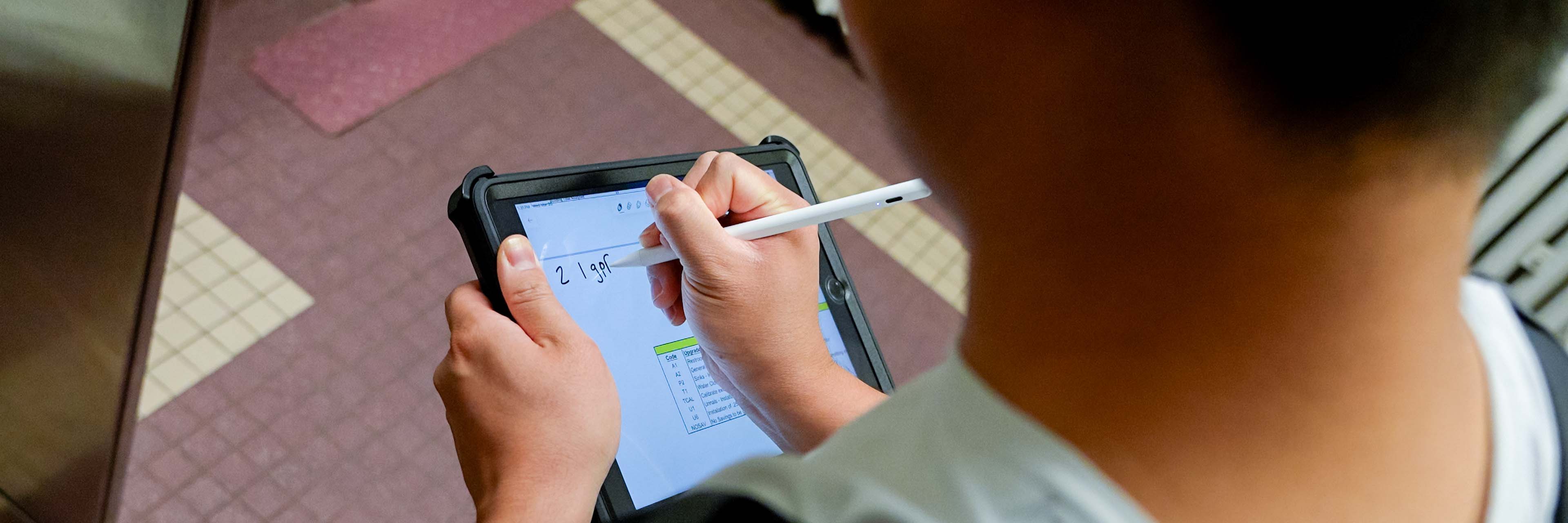 A student researcher writes on a tablet, "2 1 gpf" in a bathroom