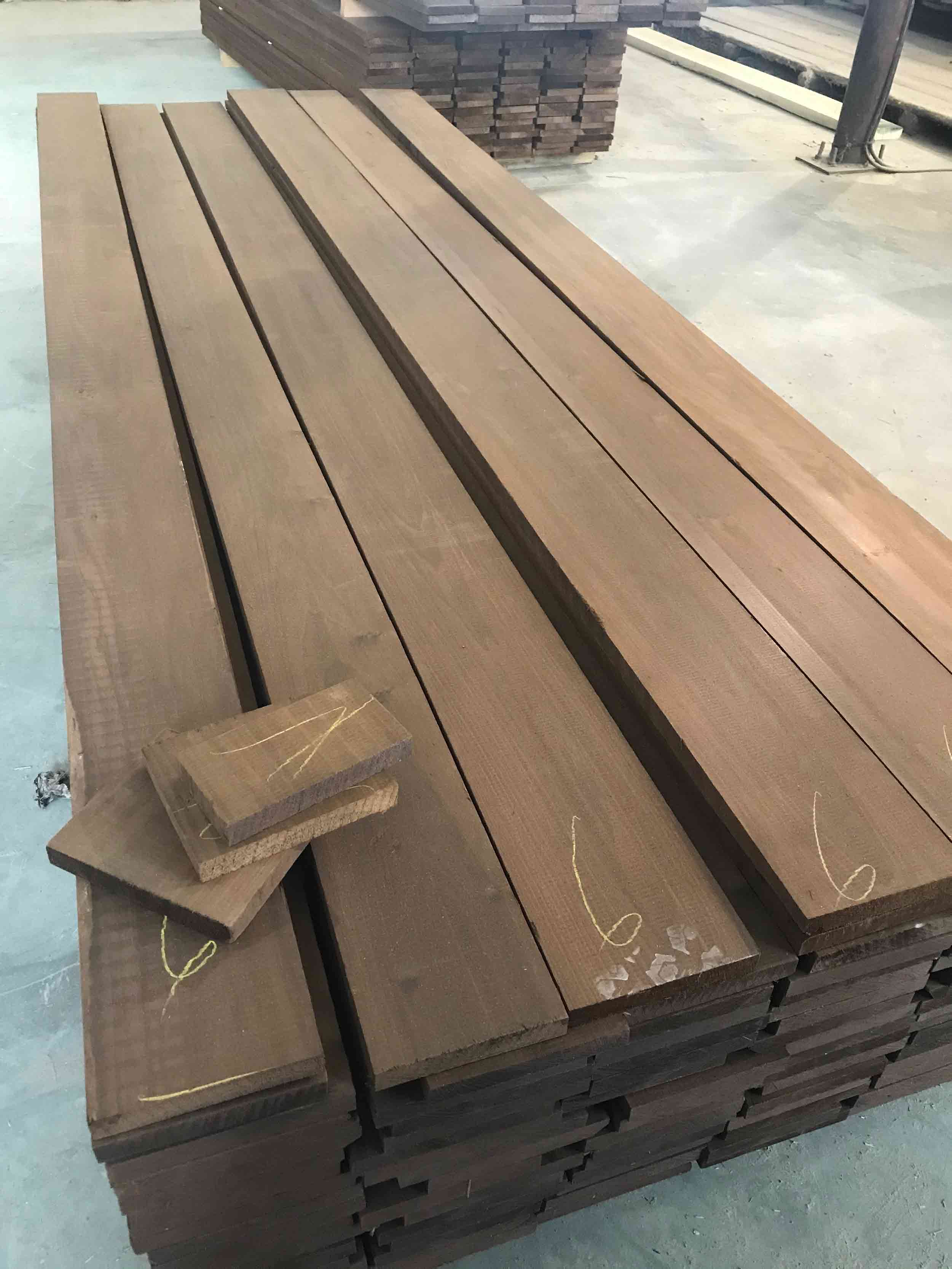 A stack of dark brown thermally modified poplar siding with the number "6" written on the end of three boards. Three smaller samples stacked upon one another with the number "7" written on top.