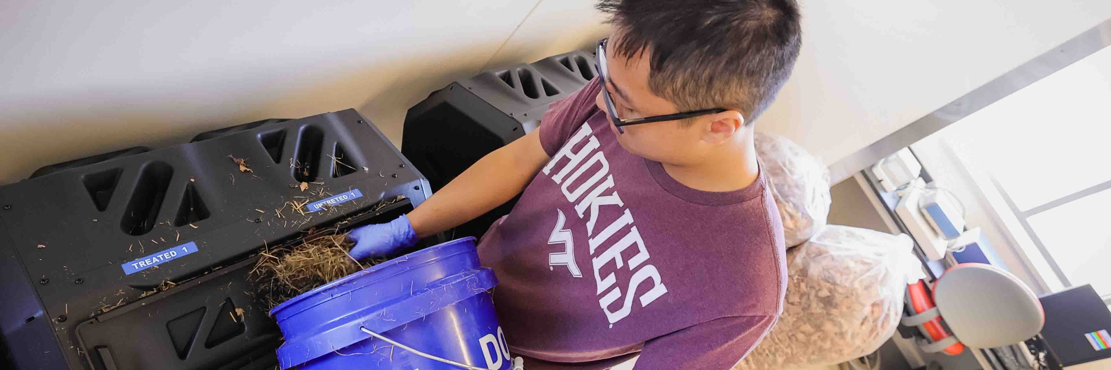 A student researcher pours straw from a bucket in to a composter