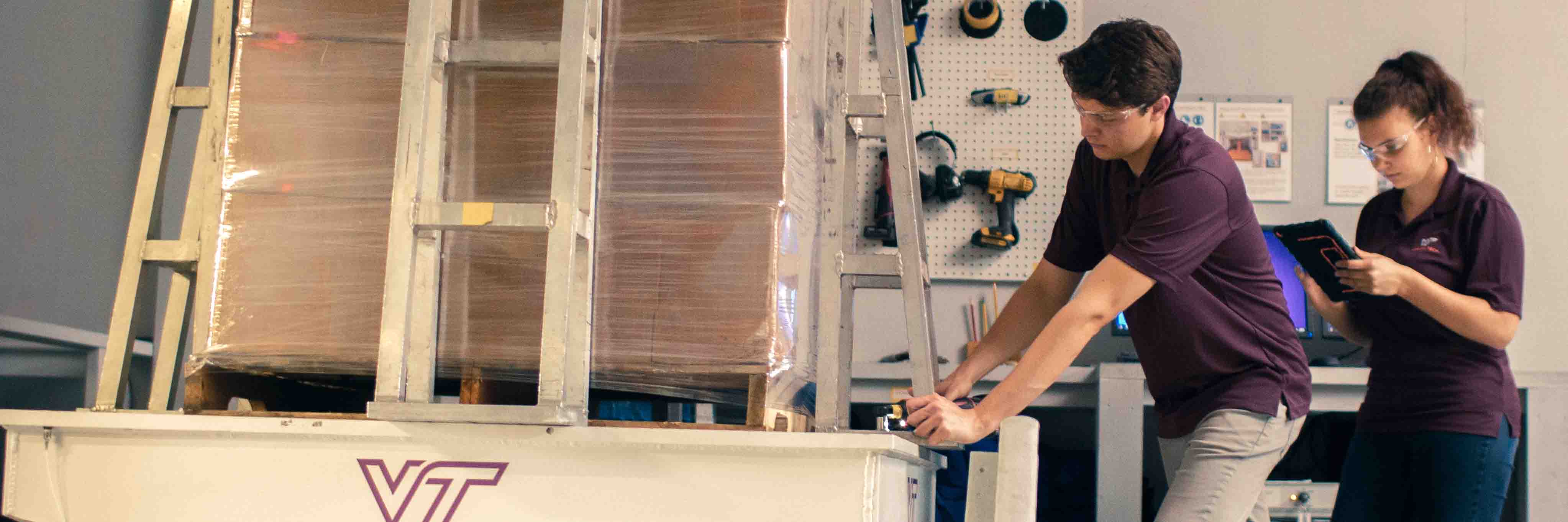 Two students preparing to test a unit load of corrugated boxes wrapped on a pallet.