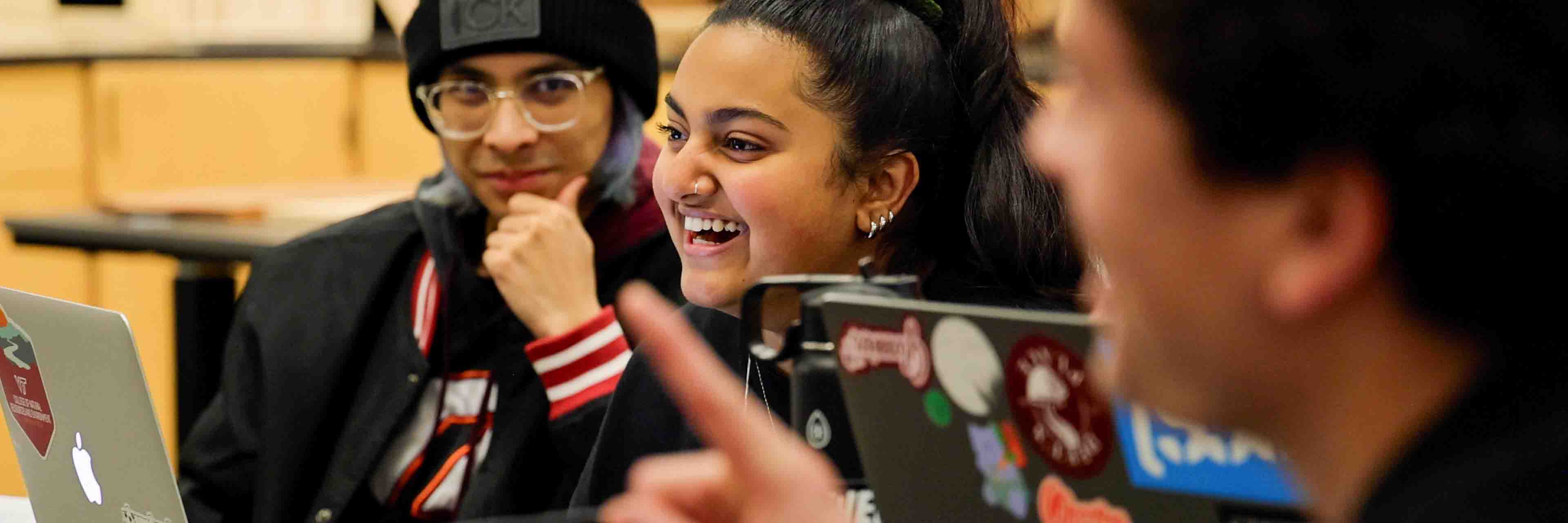 Students with open laptops in a meeting room smiling. 