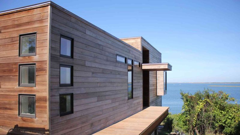 A house with thermally modified poplar siding siding, a body of water in the background.