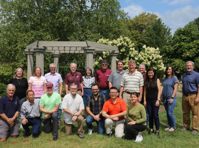 People standing and kneeling in a garden in front of a trellis
