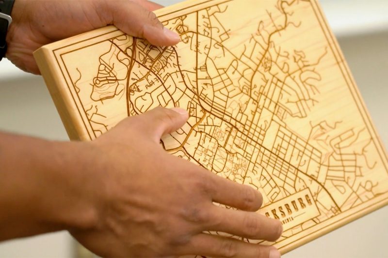 Two hands holding a map of Blacksburg laser engraved on a block of wood