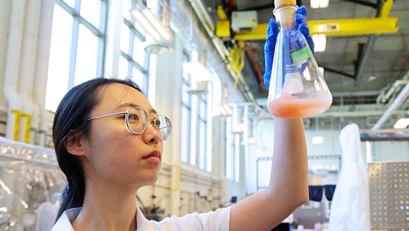 Virginia Tech sustainable biomaterials researcher in the lab holding a beaker up to eye level.