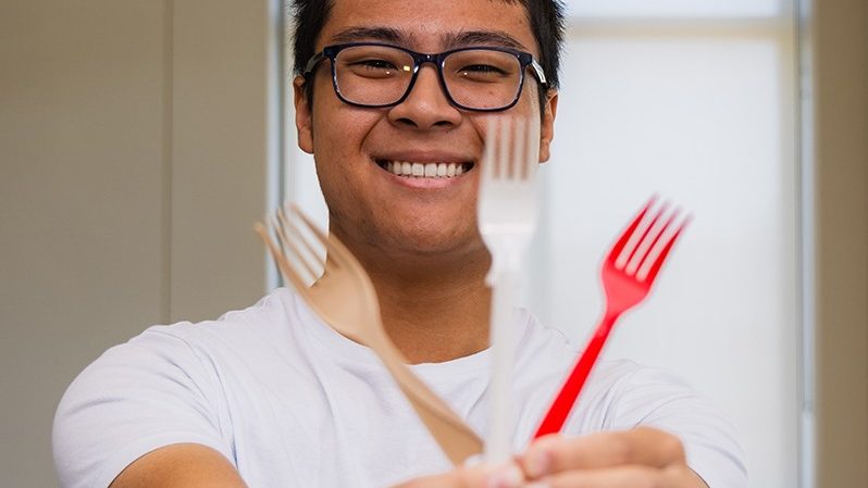 Brian Tea A sustainable biomaterials researcher holds up in front of them three forks made of different compostable material.